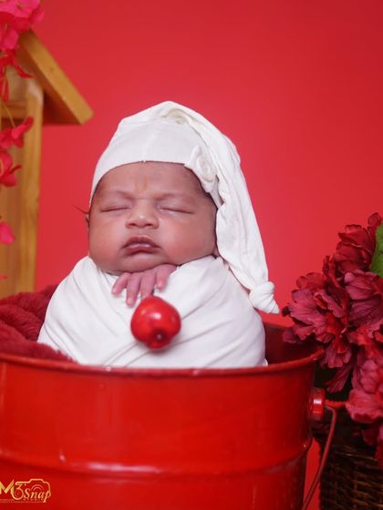 A close-up of the baby in the red bucket. His little expression is just priceless. The white sleepy hat adds a touch of whimsy.