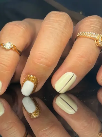 A sophisticated design with off-white nails, gold glitter accents, and fine line details.