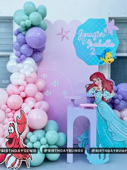 A sweet Little Mermaid setup with cutouts of Ariel and Sebastian. The balloon arch in pastel pink, purple, and mint green creates a soft and dreamy underwater feel.