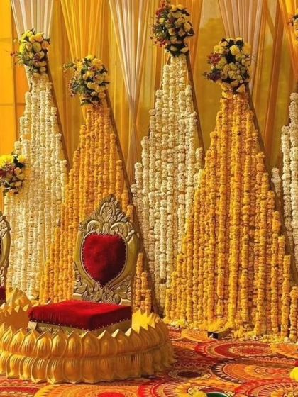 A grand Haldi seating arrangement with a backdrop of marigold and tuberose strings. The ornate golden chairs with red cushions add a royal touch to the traditional decor.