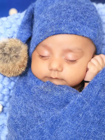 A close-up portrait of a sleeping newborn, snugly wrapped in a blue swaddle with a matching pom-pom hat. This shot highlights the delicate features and peacefulness of the baby.