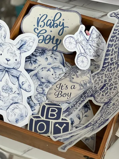 A box full of custom-designed cutouts for a baby boy hamper. These little details, like the bunny, pram, and 'It's a Boy' shoe, are what bring a theme to life.