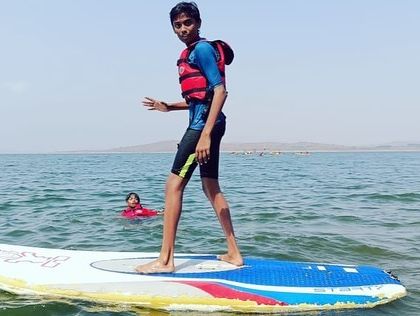 A camper enjoys the challenge of stand-up paddleboarding, with another swimmer in the background.