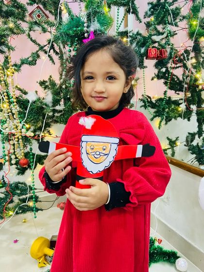 A student in a festive red dress holds up the Santa craft she made during our Christmas workshop.
