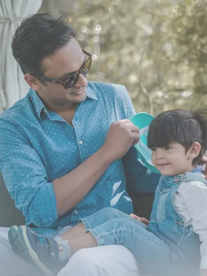 A father gently interacts with his son, who is sitting comfortably on a couch during an outdoor session.
