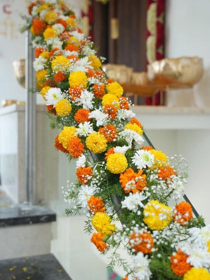 A detailed shot of a staircase railing decorated with a thick garland of yellow and orange marigolds and white chrysanthemums for a housewarming event.