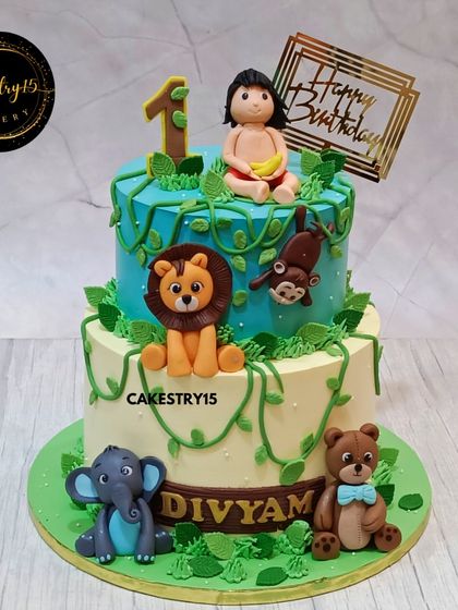 A playful two-tier jungle-themed cake for a first birthday. This cake, in black forest and butterscotch flavors, is decorated with a Mowgli-like figure and friendly jungle animals.
