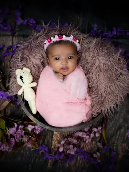 An awake and alert newborn wrapped in pink, surrounded by purple flowers. Her direct gaze is captivating.