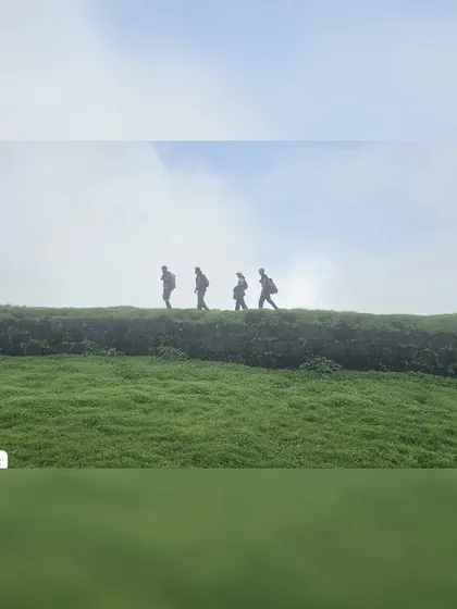 Silhouettes of trekkers walking along the wall of Korigad Fort, with misty green hills all around.