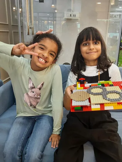 Best friends and building buddies! Two girls proudly show off their colorful LEGO creation at our workshop. These sessions are great for fostering collaboration and social skills.