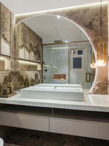 I designed this bathroom to be a luxurious escape, using dramatic, book-matched marble on the walls. The custom arched mirror and sculptural vanity create a sense of grandeur, while the warm backlighting and elegant pendant light add a soft, inviting glow.