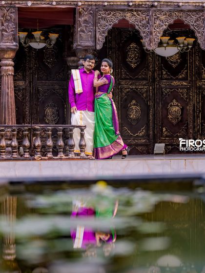 A beautiful reflection shot of the couple in traditional wear by the water, with the ornate wooden doors in the background.