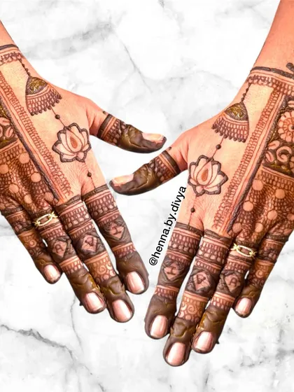 A unique back-hand design with a central panel featuring lotus motifs and hanging jhumkas. The fingers are adorned with hearts and initials for a personal touch.
