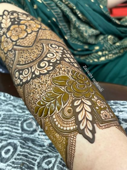 A close-up of the fresh henna paste on Nazreen's arm, showing the texture and dimension of the design.