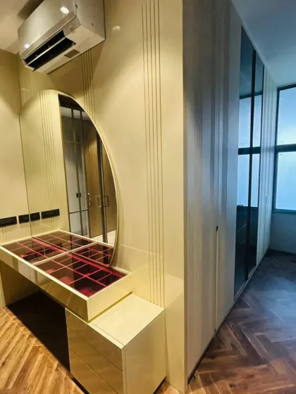 This bedroom corner combines a custom dressing vanity and a full-height wardrobe. The vanity includes a glass-top display for organized jewelry storage, while the entire setup is finished in a high-gloss laminate for a sleek, modern look.