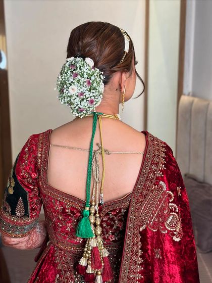 This bridal bun is adorned with a full gajra of baby's breath and small pink flowers, creating a delicate and ethereal look for the bride's special day.