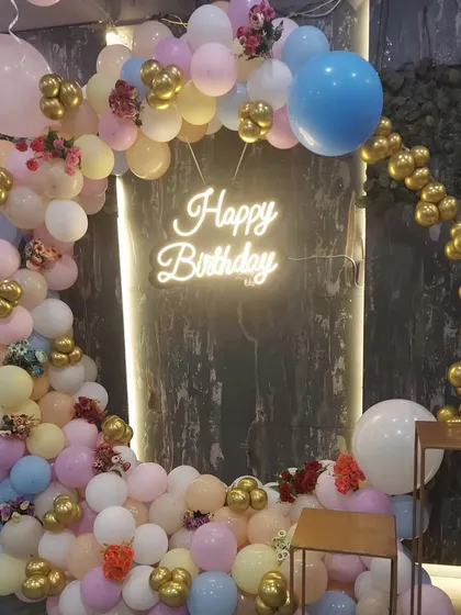 A closer look at a pastel-themed birthday balloon arch. This circular arrangement combines soft pink, blue, and yellow balloons with pops of gold chrome and small floral details for an elegant finish.