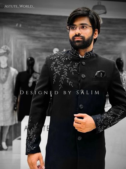 A client in a black sherwani-style jacket with intricate silver embroidery on the shoulder and cuffs. This is a sharp and elegant choice for a groom or wedding guest.