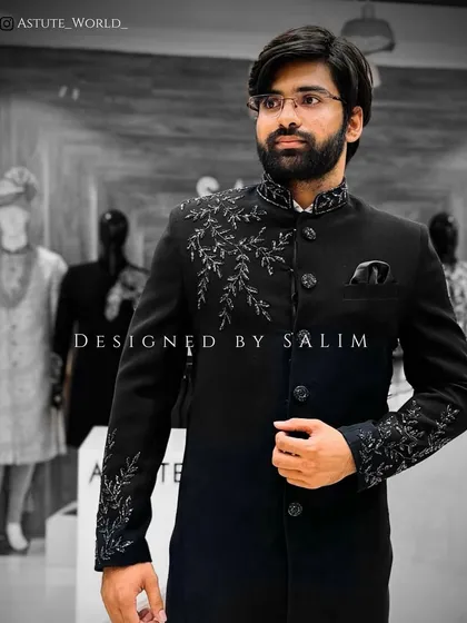 A client in a black sherwani-style jacket with intricate silver embroidery on the shoulder and cuffs. This is a sharp and elegant choice for a groom or wedding guest.