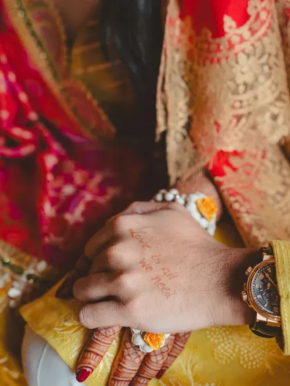 A close-up of the groom's hand with "Love is all we need" written on it, a sweet, personal detail from their Haldi.