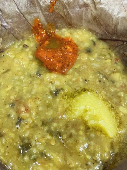 A healthy and comforting bowl of vegetable daliya (savory porridge). It's topped with a dollop of ghee and a spoonful of spicy pickle.