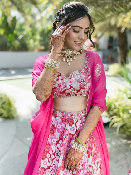 The bride's soft, braided updo complements her floral lehenga and glowing makeup, creating a fresh and youthful pre-wedding look.