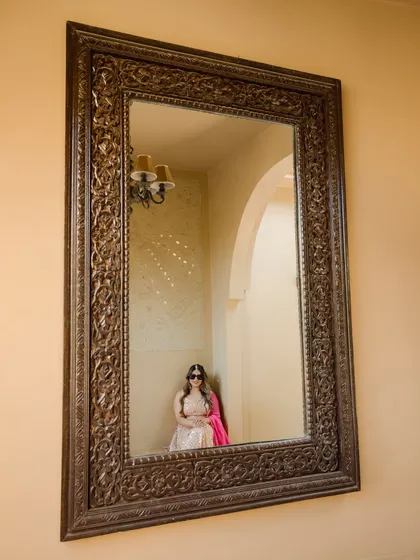 An artistic shot of the bride reflected in an ornate mirror. This creative composition adds a touch of elegance and introspection to her Mehendi portraits.