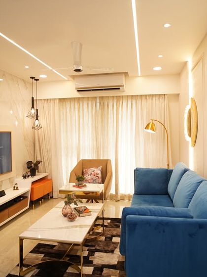 A wide shot of a completed living room, ready for the clients to move in. The combination of a blue sofa, marble-finish TV wall, and warm lighting creates a welcoming space.
