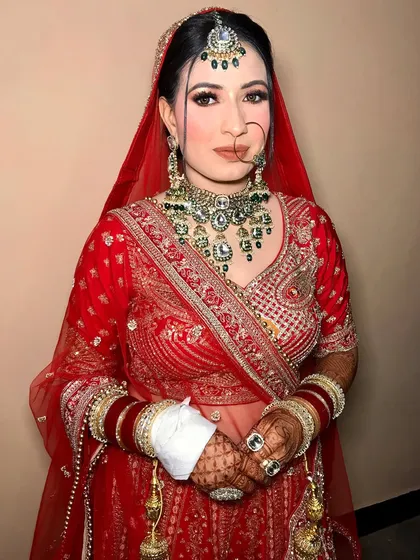 This bride is wearing a coral-red lehenga, beautifully styled with a heavy kundan and emerald jewelry set.