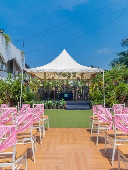 A beautiful daytime ceremony setup in the Terrace Garden, with pink chair decor and a tented stage surrounded by greenery.