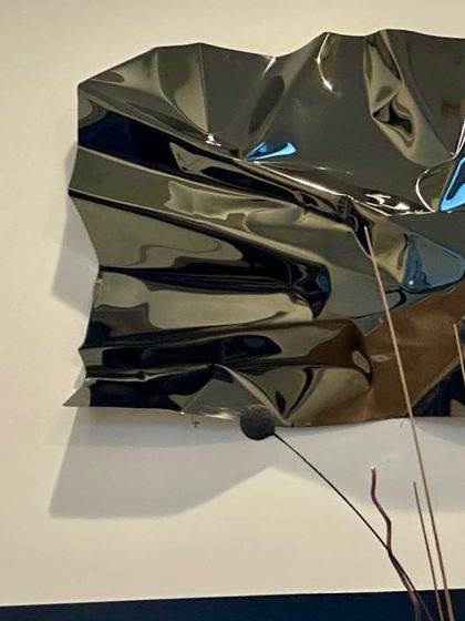 The glossy black finish reflects the light in unexpected ways, creating highlights that define its crumpled form.