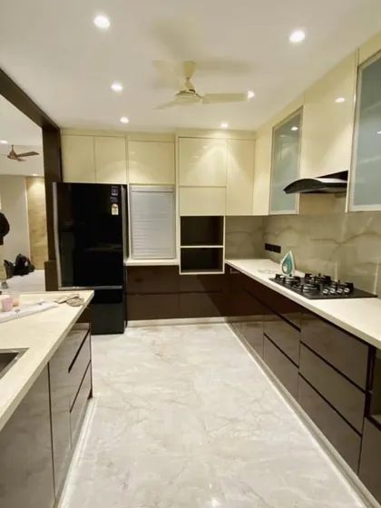 A spacious U-shaped kitchen with a dual-tone design, combining rich brown base cabinets with cream-colored upper cabinets. The layout includes a rolling shutter unit and glass-fronted cabinets.