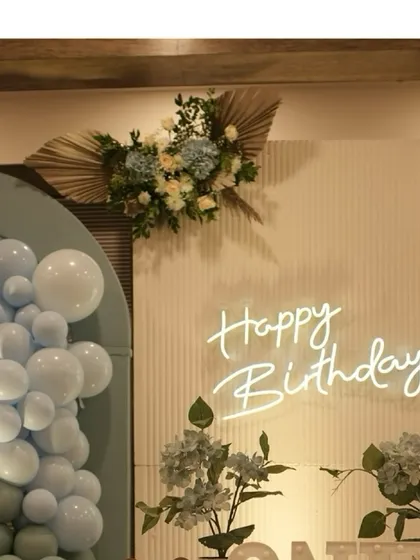 A modern and chic birthday backdrop we designed, featuring a custom "Happy Birthday" neon sign against a textured panel. The look is completed with a stylish balloon arrangement and dried floral accents for a trendy yet timeless feel.