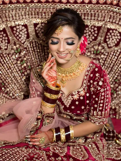 A candid shot of a bride seated, looking down with a smile. The makeup is soft and romantic, perfect for this velvet lehenga.