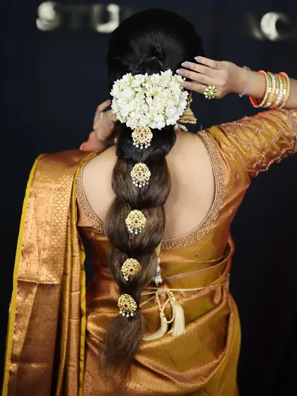 A detailed view of a traditional South Indian bridal braid, adorned with beautiful gold accessories and fresh jasmine flowers (gajra).