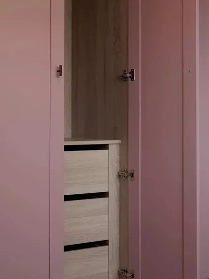 A close-up of the wardrobe's interior, showing the handleless drawers and the contrast between the pink exterior and the light wood-grain finish inside.