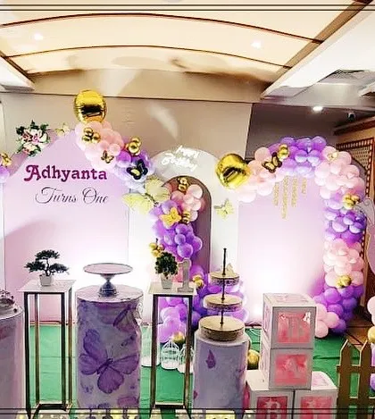 An elegant butterfly garden theme for a first birthday party. This setup uses a soft purple and pink color palette with beautiful balloon arches, large butterfly wing cutouts, and themed pedestals for the cake display.