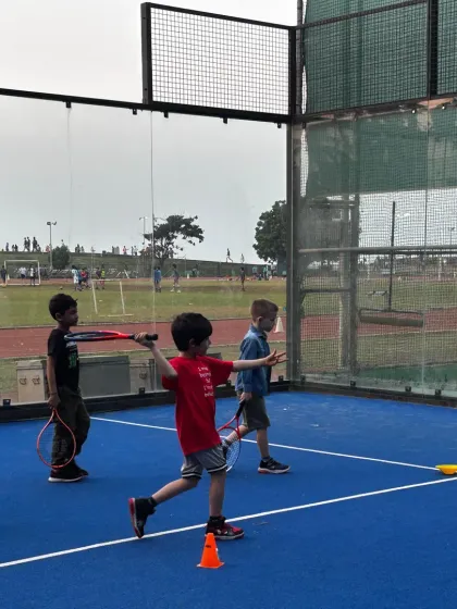 We focus on teaching the correct form from day one. In this shot, you can see young players practicing their swing technique under the watchful eye of a coach on our vibrant blue courts.