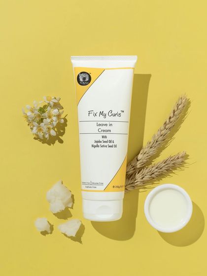 A warm, monochromatic flatlay that uses a sunny yellow background. The ingredients like wheat and coconut are arranged to complement the leave-in cream, creating a harmonious and cheerful image.
