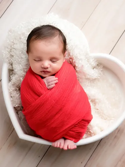 The cutest little one nestled in a heart-shaped bowl. The bold red wrap adds a pop of color while keeping the focus on the baby's peaceful expression.
