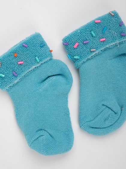 A product shot of the matching blue baby socks with colorful sprinkle details.