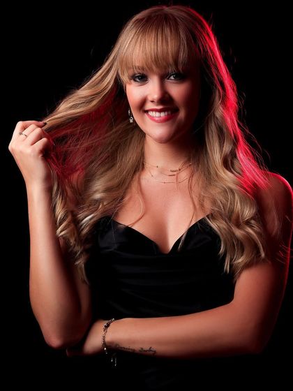 A smiling portrait of a model against a black background, with a soft red backlight adding a touch of color and warmth.