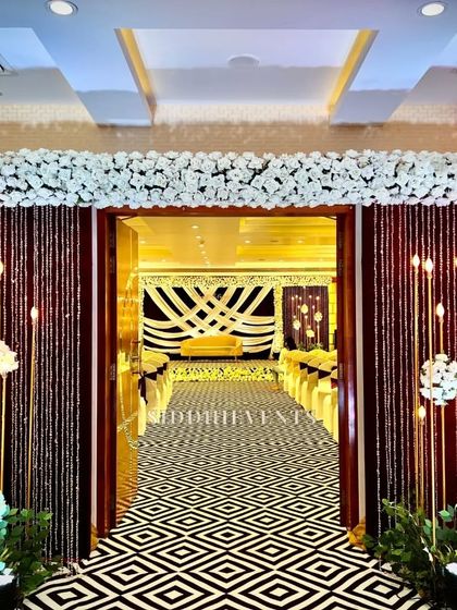 An elegant entrance with a black and white geometric carpet, leading into a hall decorated in a sophisticated brown and white theme with beautiful lighting.