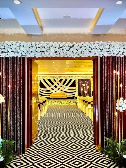An elegant entrance with a black and white geometric carpet, leading into a hall decorated in a sophisticated brown and white theme with beautiful lighting.