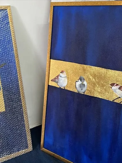 A pair of my bird paintings, featuring blue jays and sparrows on gold leaf bands, displayed in a client's bedroom. The deep blue background creates a rich, luxurious feel.