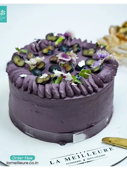 A beautiful Blueberry Cake with a lovely lavender-hued frosting. It's decorated with fresh blueberries and edible flowers for a simple yet elegant look.