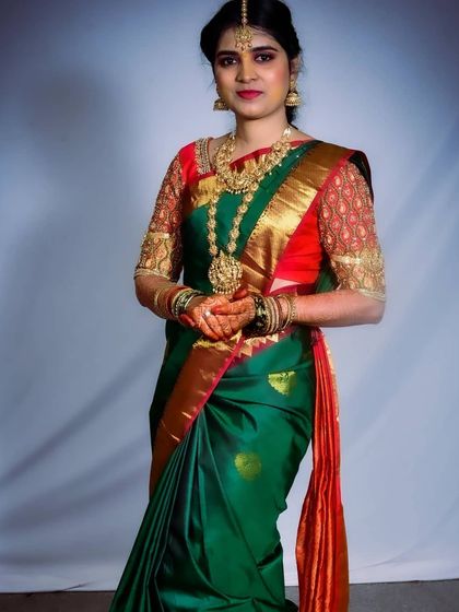 A classic South Indian engagement look. The bride is wearing a beautiful green silk saree with a contrasting red blouse, and her makeup features traditional gold jewelry and a defined eye.