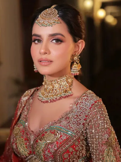 A classic bridal portrait. The styling focuses on the harmony between the heavy gold jewelry and the rich red tones of the lehenga.