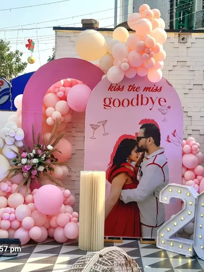 A fun and chic backdrop for a bachelorette party or bridal shower. The "kiss the miss goodbye" theme is brought to life with pink balloon arches and a light-up age number.