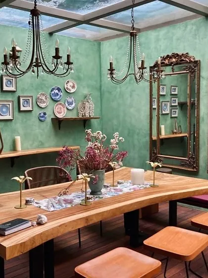 We designed this dining space within a glass-enclosed conservatory to feel both rustic and refined. A live-edge wooden table serves as the centerpiece, complemented by ornate mirrors and classic chandeliers, creating an elegant dining experience under a transparent skylight.
